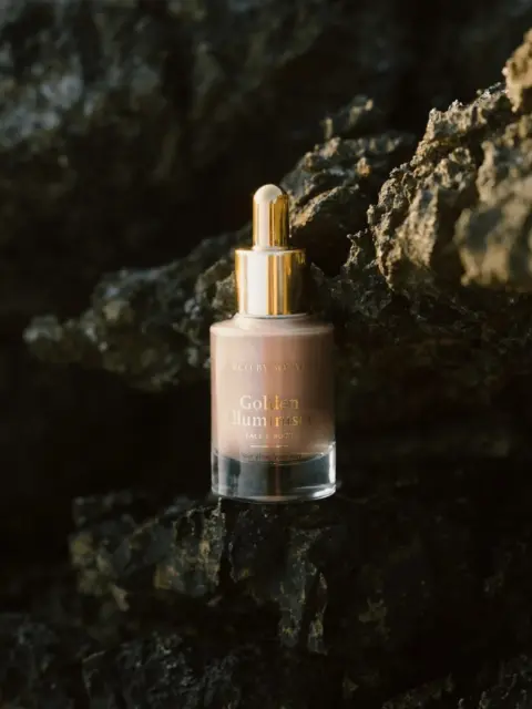 Golden serum bottle with dropper on dark rocks.