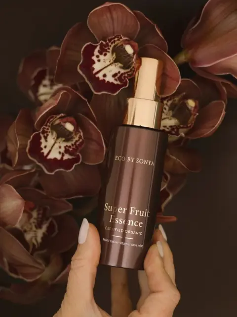 Brown bottle of Super Fruit Essence held in front of dark orchids.
