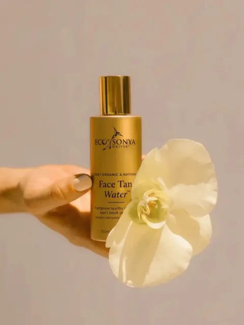 Eco by Sonya Face Tan Water bottle held with a white orchid.