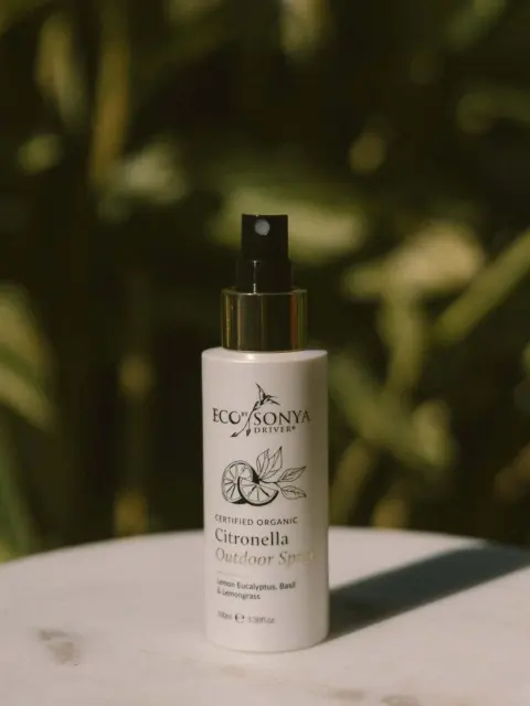 Eco Sonya Citronella Outdoor Spray bottle on a marble surface, green foliage background.