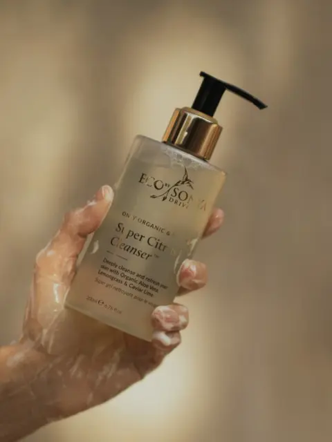 Hand holding Eco by Sonya Super Citrus Cleanser bottle.