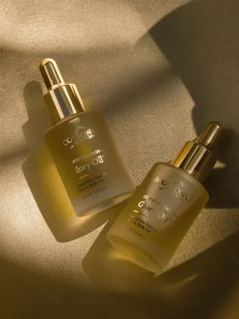 Two bottles of Eco Sonya Glory Oil on a gold surface, with dropper caps.