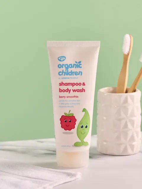 Organic Children shampoo and body wash tube on marble surface, toothbrushes in holder nearby.