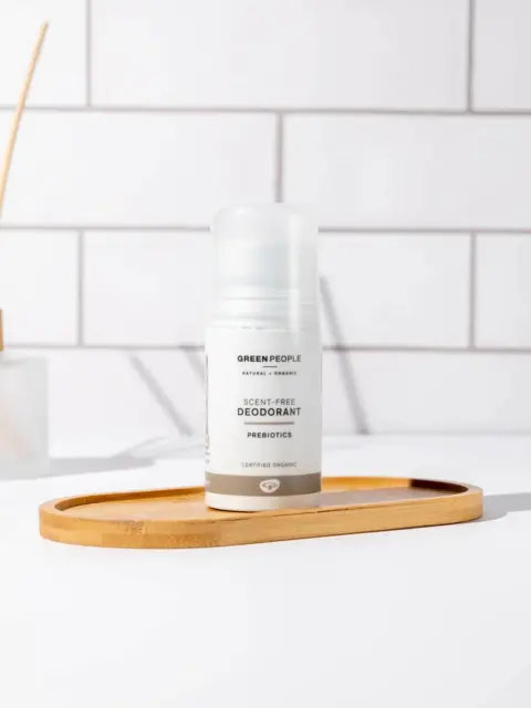 Scent-free deodorant on wooden tray, white tiled background.