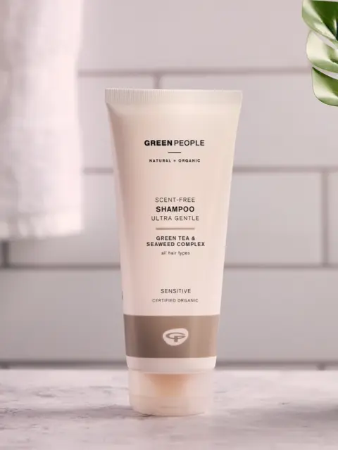 Green People scent-free shampoo tube on a bathroom counter with a plant and towel nearby.