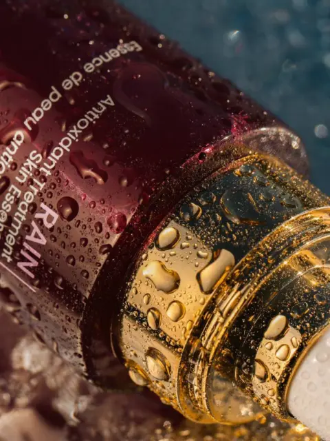 Skincare serum bottle with water droplets on a textured surface.