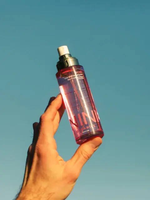 Hand holding a pink spray bottle against a clear blue sky.