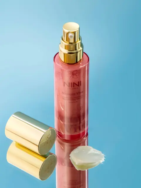 Red spray bottle with gold cap on blue background, cream smear beside it.