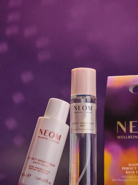 Neom Wellbeing bath foam and mist with packaging on a purple background.
