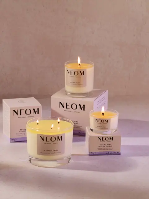 Lit NEOM candles with packaging on a light surface.