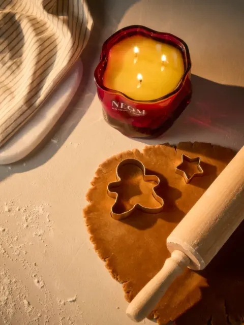 Red candle labelled "NEOM", dough with cutters, rolling pin, and striped cloth.