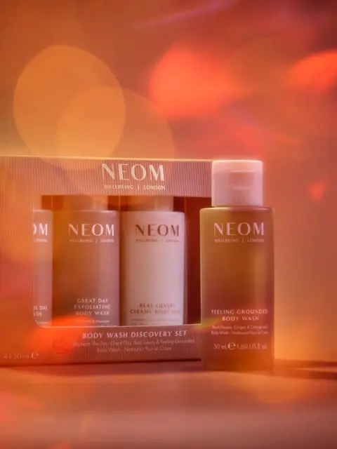 NEOM Body Wash Discovery Set with three bottles against a warm, blurred background.