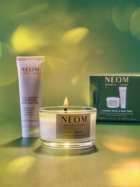 Neom candle, body butter, and gift box on a green background with soft light effects.