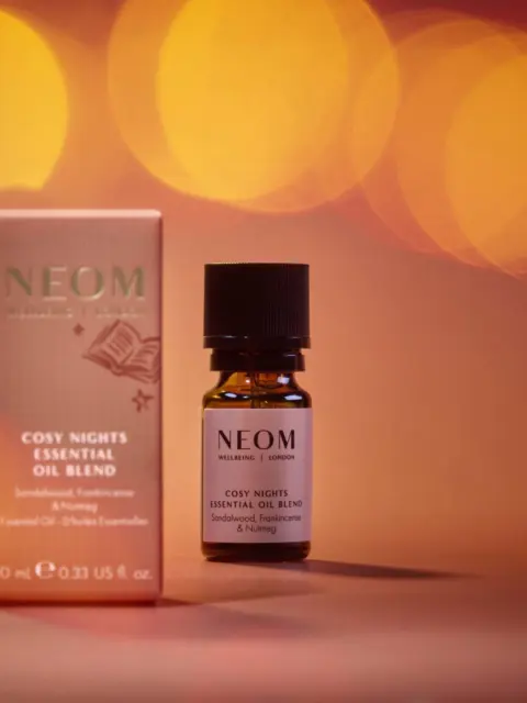 NEOM Cosy Nights Essential Oil Blend with packaging, 10ml bottle, warm bokeh background.