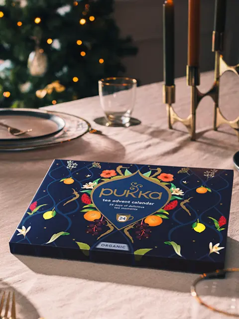 Tea advent calendar on a dining table with lit candles and a Christmas tree in the background.