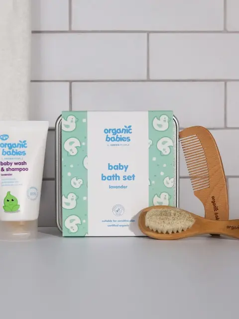 Baby bath set with lavender wash, wooden comb, and brush on a tiled background.