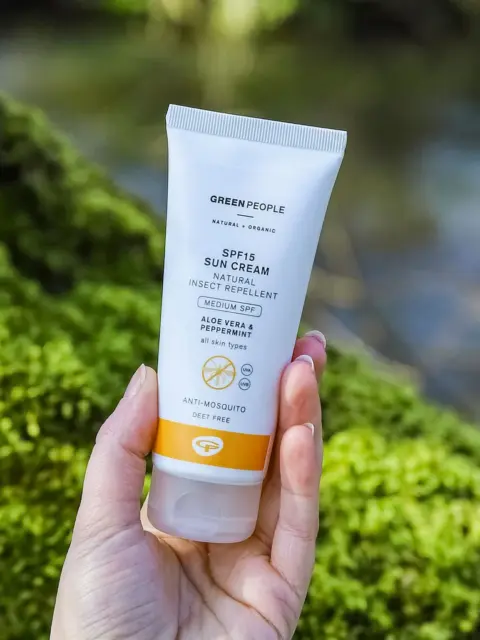 Hand holding Green People SPF15 sun cream tube outdoors.