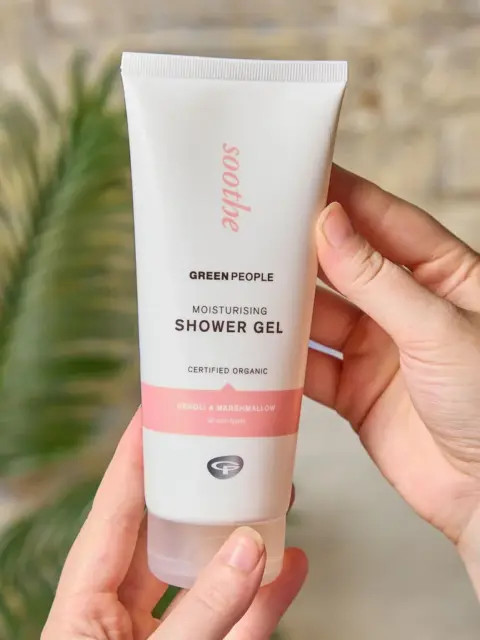 Hands holding Green People moisturising shower gel tube.