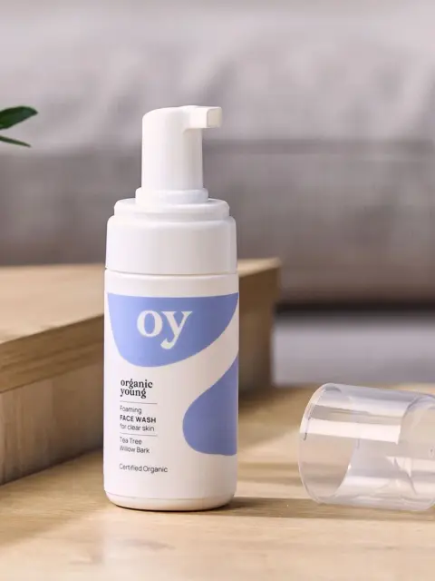 Organic Young foaming face wash on wooden surface, cap off, with plant in background.