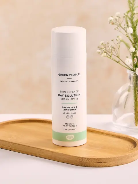 Skincare cream bottle on wooden tray, labelled "Green People Skin Defence Day Solution SPF 15".