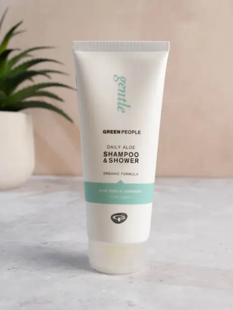 Green People Daily Aloe Shampoo & Shower tube on a marble surface, plant in background.