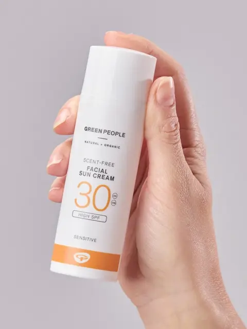 Hand holding Green People SPF 30 scent-free facial sun cream bottle.