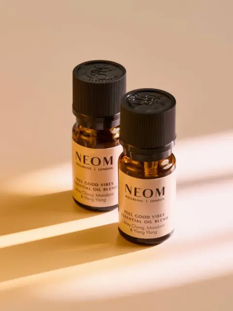 Two NEOM essential oil bottles on a beige surface with light stripes.