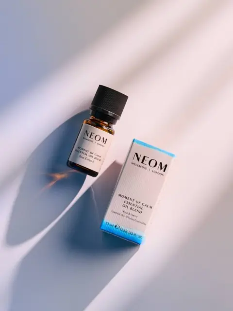 Neom essential oil bottle and box on a light surface with shadows.