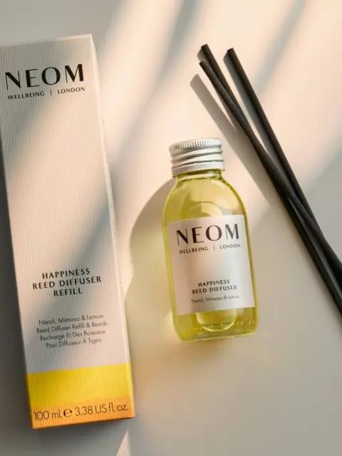 NEOM Happiness Reed Diffuser Refill with bottle and black reeds on a light surface.