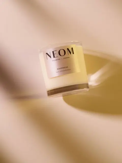 NEOM candle labelled "Happiness" on a beige background.