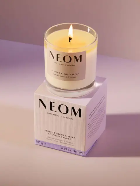 Lit NEOM scented candle on box, labelled "Perfect Night's Sleep".