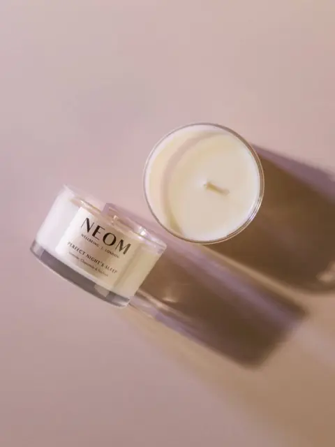 Two NEOM candles on a beige surface, one with a lid and one open.