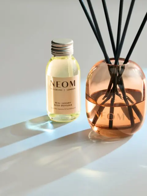 Neom reed diffuser and oil bottle on a light surface.
