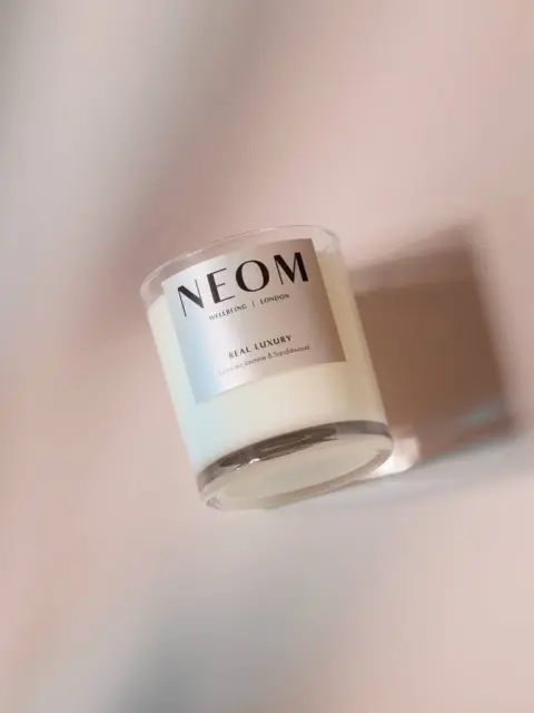 White NEOM candle with "Real Luxury" label on a soft pink background.
