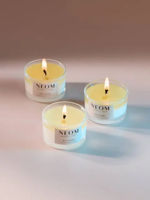 Three lit NEOM candles on a smooth surface.