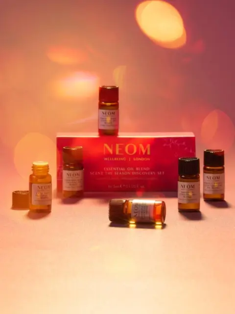 NEOM essential oil set with six small bottles on a pink surface, warm lighting.
