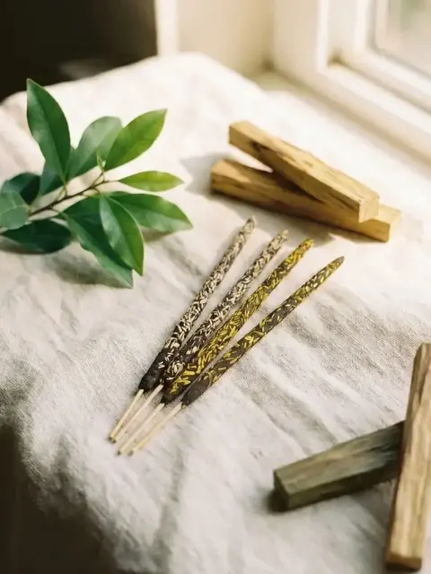 Incense sticks, wooden blocks, and green leaves on a linen cloth by a window.