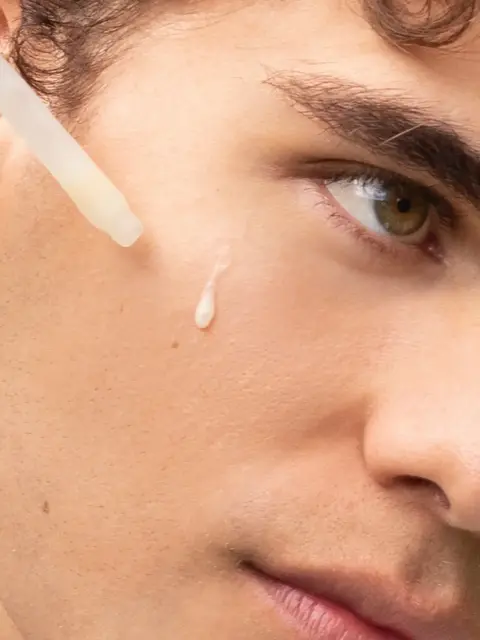 Dropper applying serum to a person's cheek.