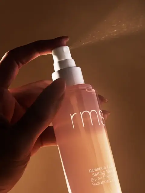 Hand spraying rms Radiance Lock Setting Mist in warm lighting.