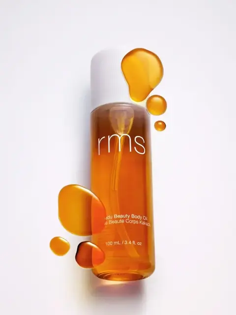 RMS Kakadu Beauty Body Oil, 100 mL bottle with oil droplets on white background.