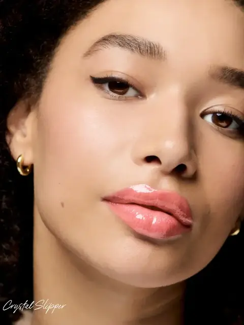 Close-up of a person with glossy pink lips, winged eyeliner, and gold hoop earrings.
