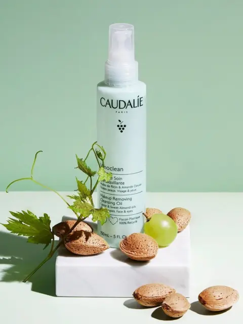 Caudalie cleansing oil bottle with almonds and grape on a white block.