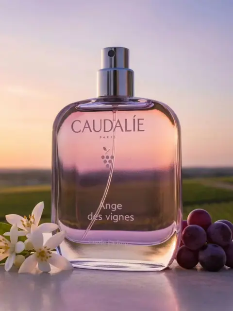 Perfume bottle labelled "Caudalie Ange des vignes" with flowers and grapes, vineyard background.