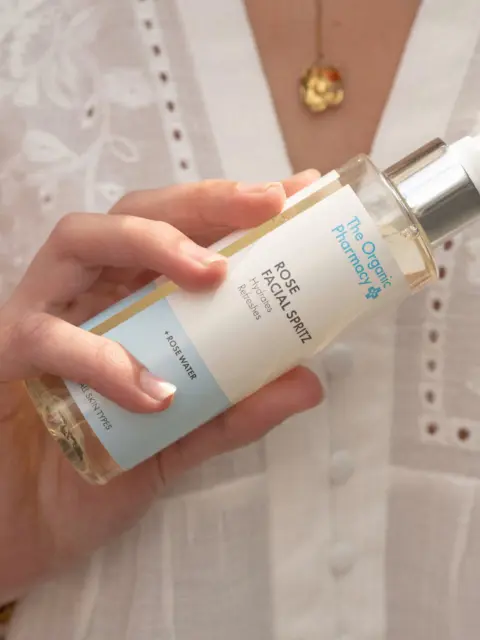 Hand holding The Organic Pharmacy Rose Facial Spritz bottle.