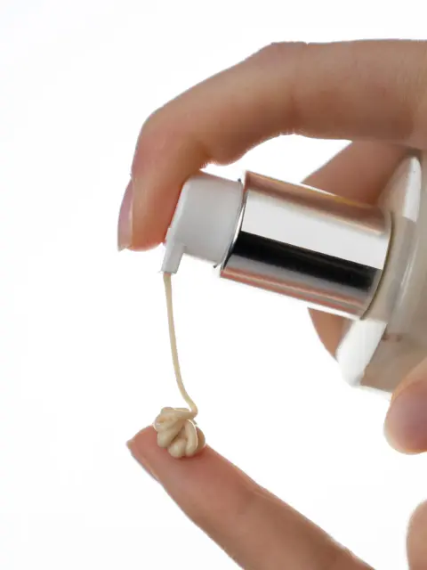 Hand dispensing cream onto fingertip from a pump bottle.