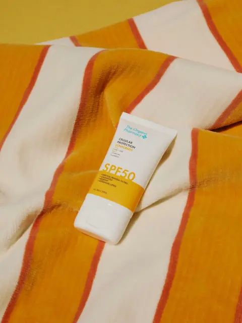 SPF 50 sunscreen tube on a striped orange and white fabric background.
