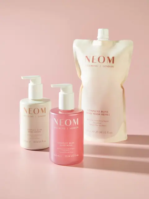 NEOM Complete Bliss hand wash, lotion, and refill pouch on a pink background.