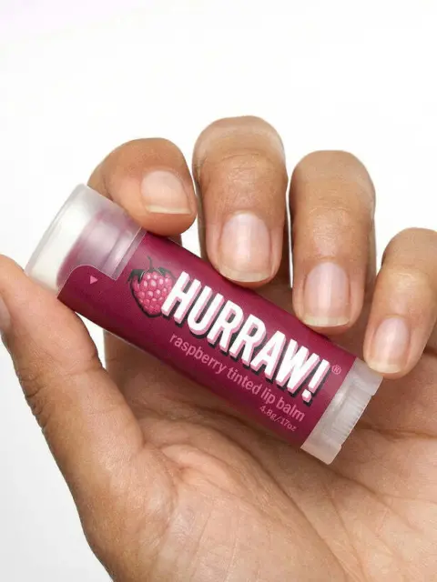 Hand holding Hurraw! raspberry tinted lip balm.
