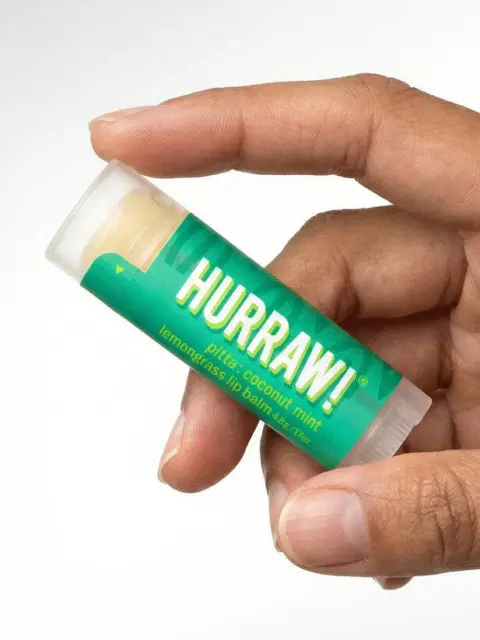 Hand holding Hurraw! lemongrass lip balm tube.