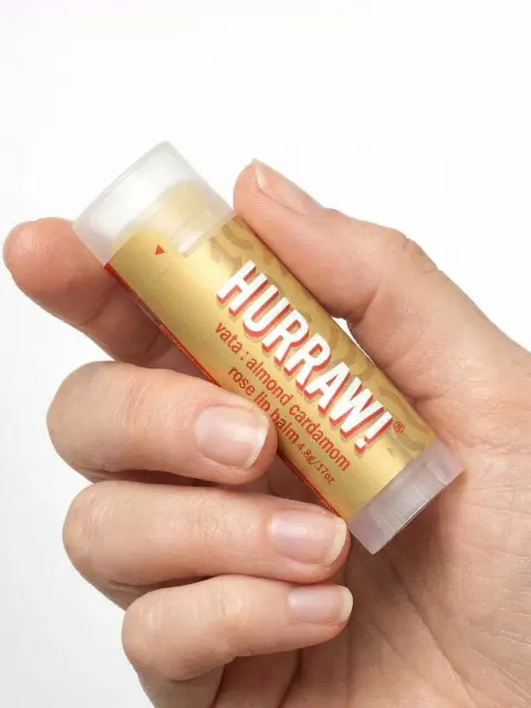 Hand holding Hurraw! almond cardamom rose lip balm tube.